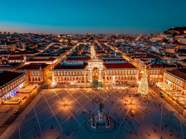 Stunning aerial view of Praça do Comércio in Lisbon, Portugal at night. The square is beautifully illuminated, showcasing city architecture and holiday decorations.